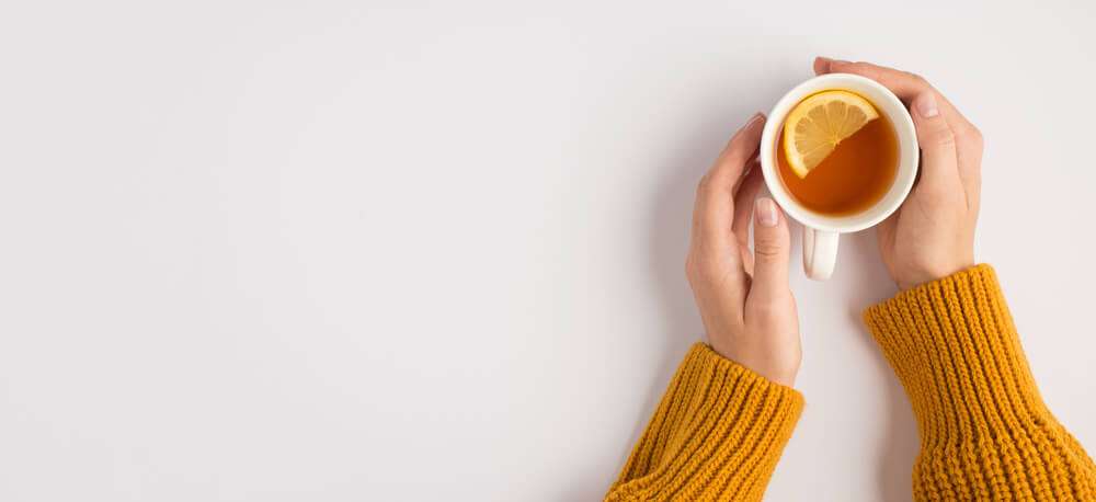 a woman with a orange sweater holding a cup of tea