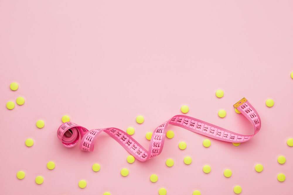 Weight measuring tape and pills in a pink background