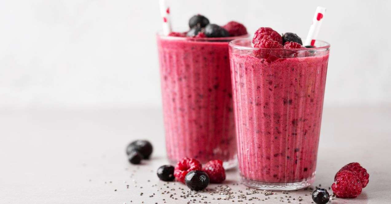 Two glasses of berry smoothie next to some berries in the white background