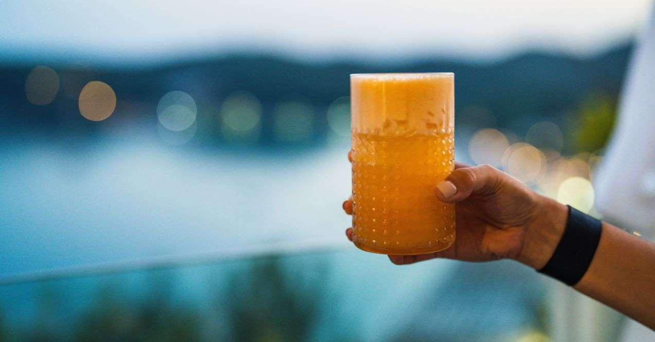 A hand holding a glass of orange juice in a panoramic view