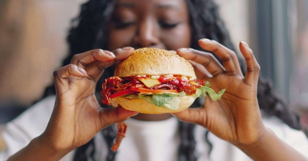 An African woman holding a burger with both hands zoomed in