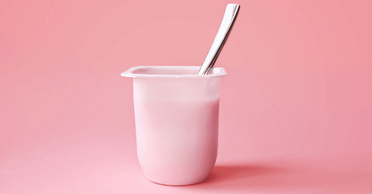 Opened pink plastic package with yoghurt and metal teaspoon inside in the pink background