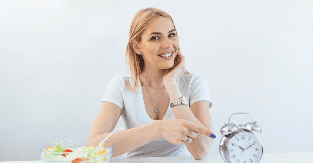 Retro alarm clock in which woman make fasting with a healthy food of salad.