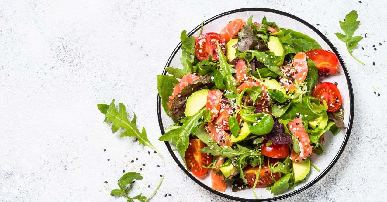 A plate of salad with salmon, tomatoes, arugula and spinach