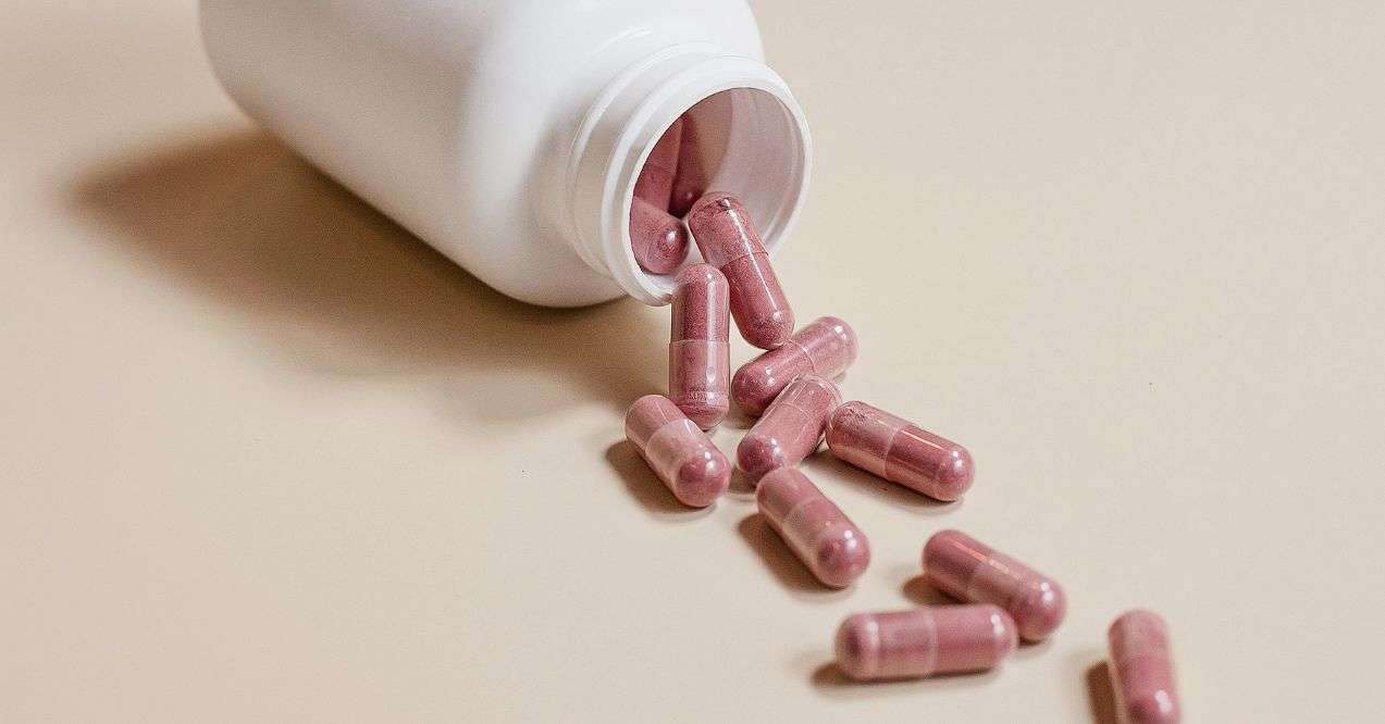 Brown pills scatterred next to a white supplement bottle