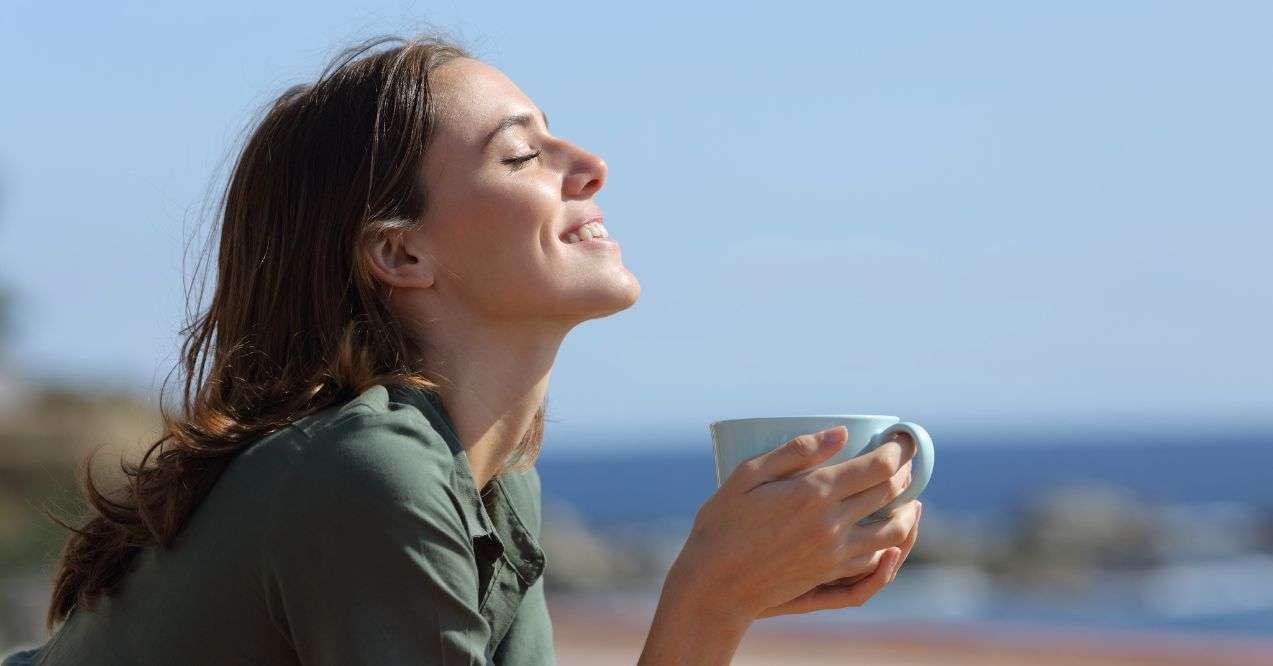 Profile of a happy woman holding coffee mug breathing fresh air on the beach.