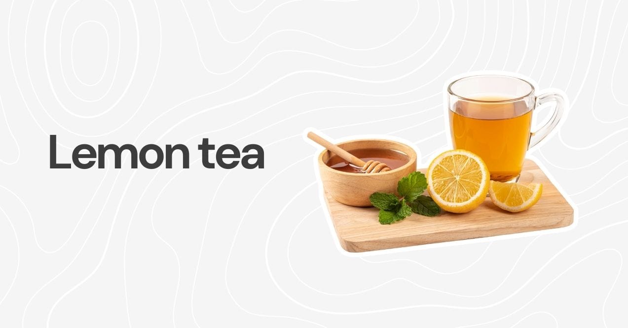 A glass cup of lemon tea with lemon slices, mint leaves, and honey on a wooden board.