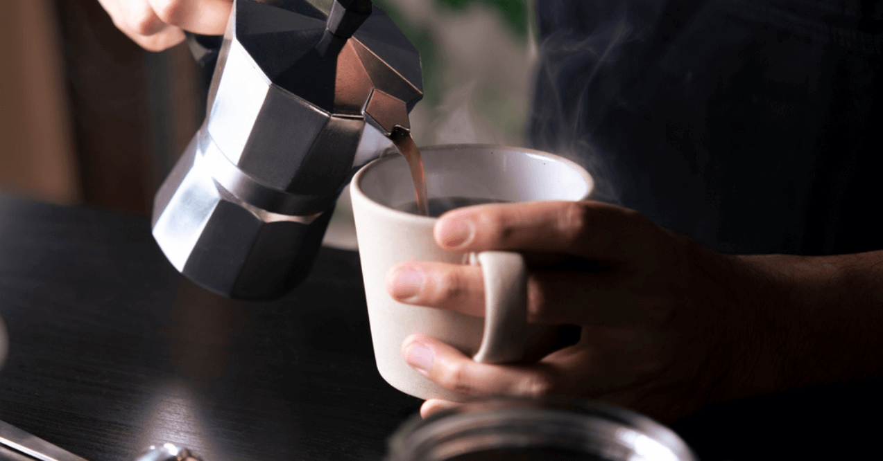 Barista pouring coffee from a pot to a coffee cup.