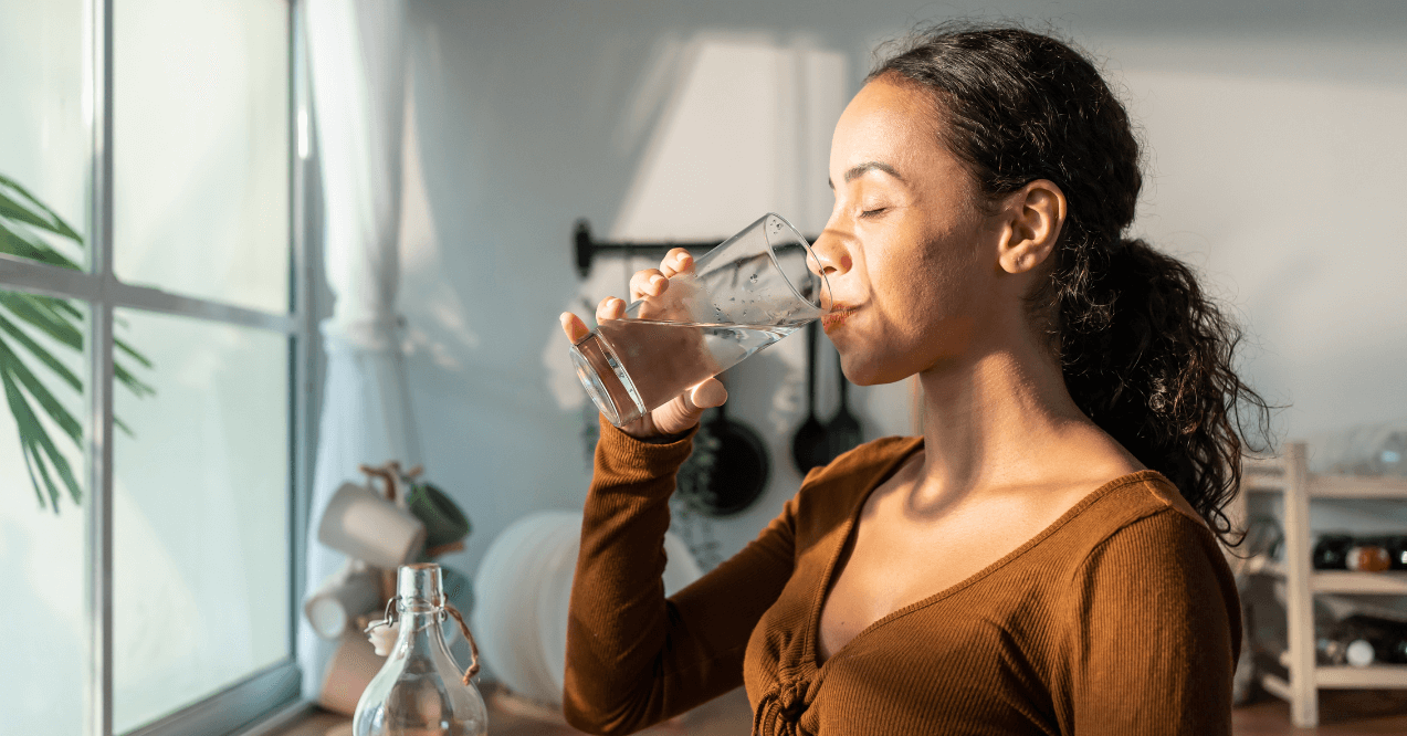 Young beautiful woman holding clean water into glass in kitchen. 