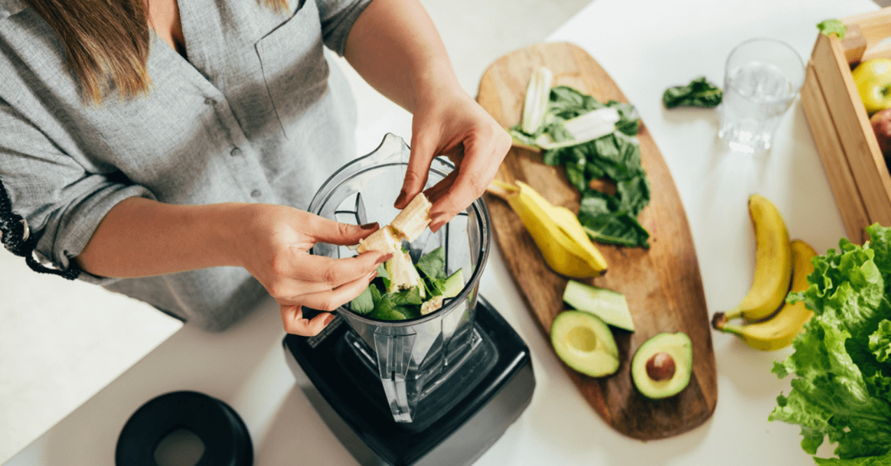 Woman is preparing a healthy detox drink in a blender - a green smoothie with fresh fruits, green spinach and avocado.