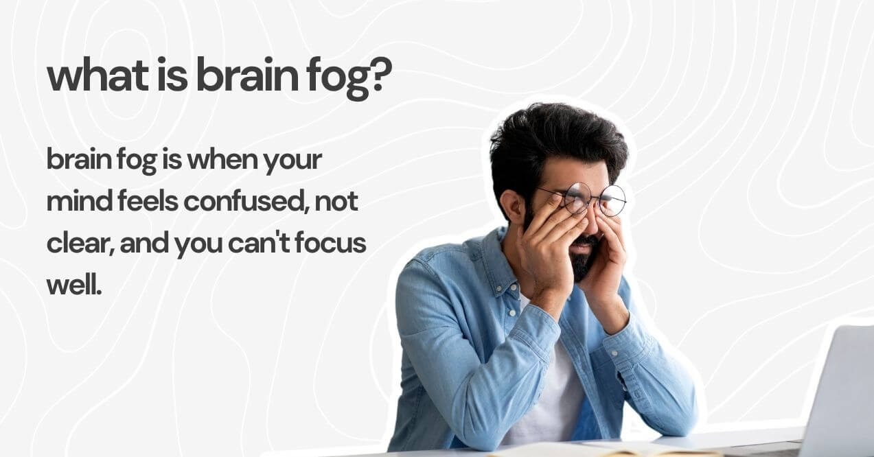 Man in glasses rubbing his eyes while sitting at a laptop, representing symptoms of brain fog.