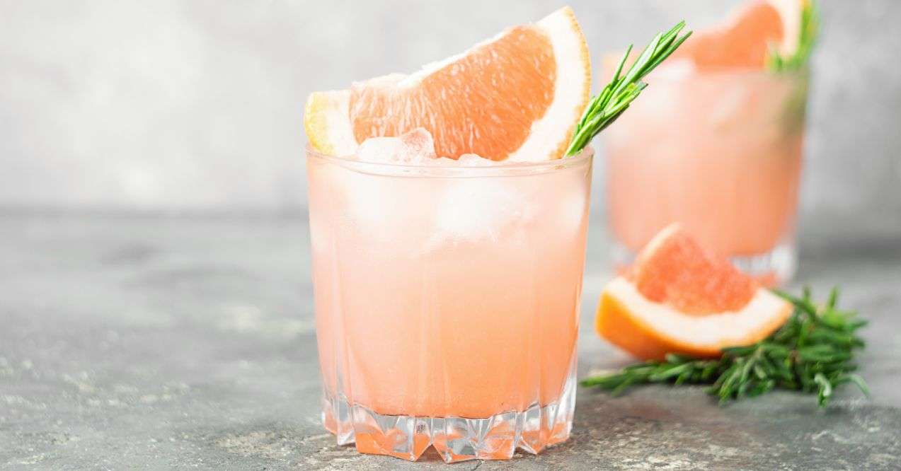 A refreshing summer cocktail of grapefruit rosemary and ice juice in elegant glass goblets on gray concrete background.