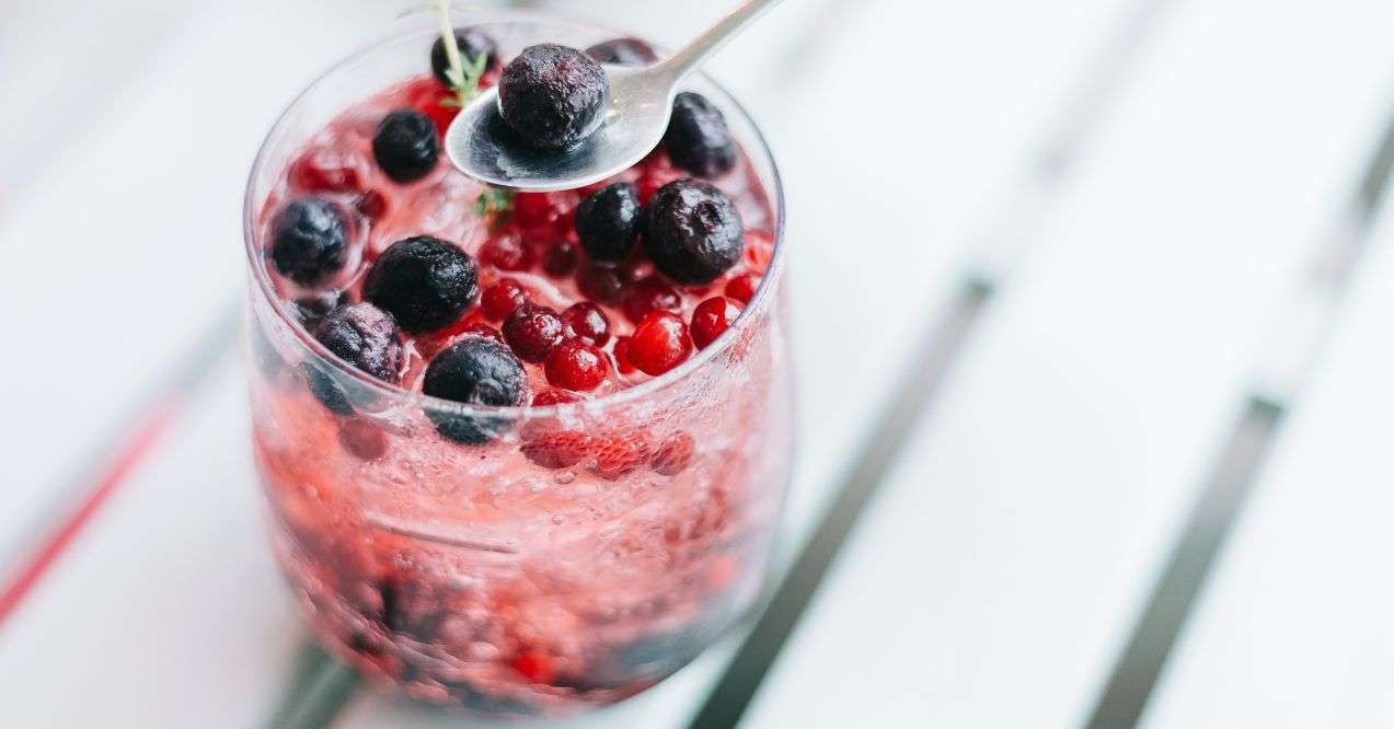 berry soda in a glass on a white wooden counter with a metal spoon