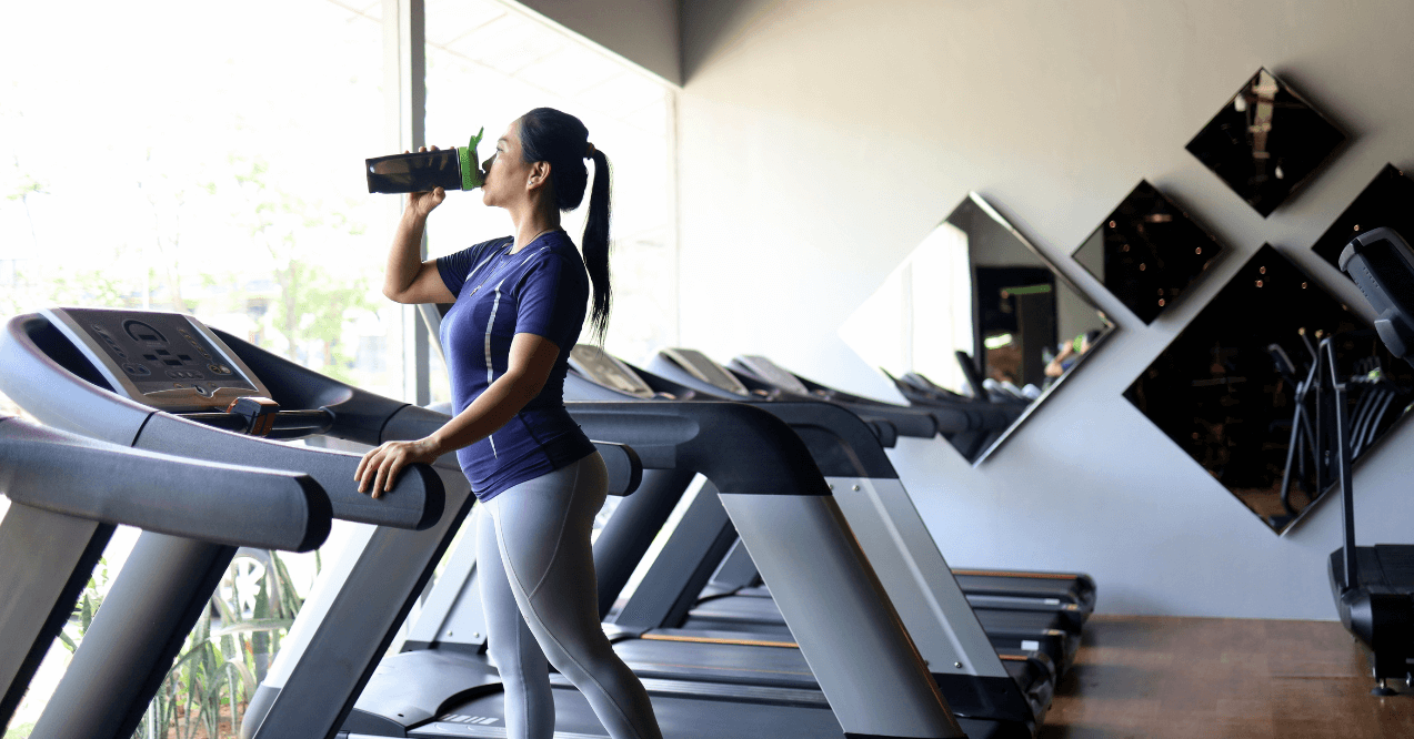 Woman on a treadmil drinking pre-workout and looking through the window