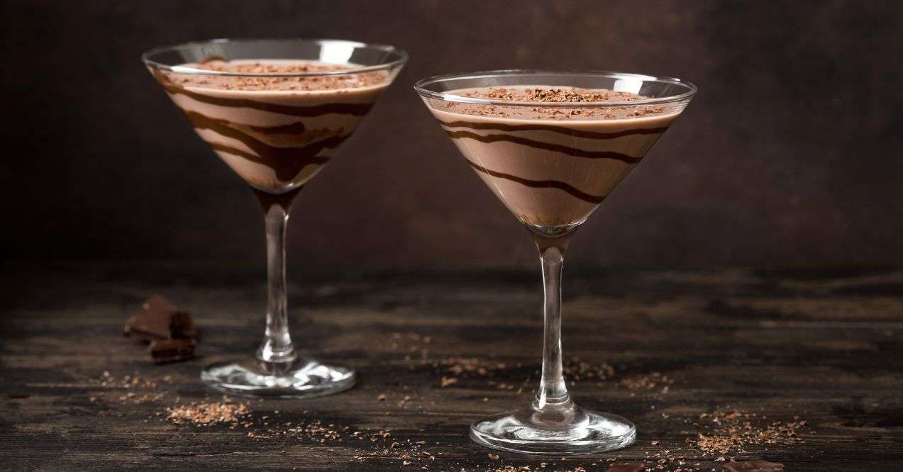 Two martini glasses with coffee mocktail with cream and chocolate inside. Wooden background, dark