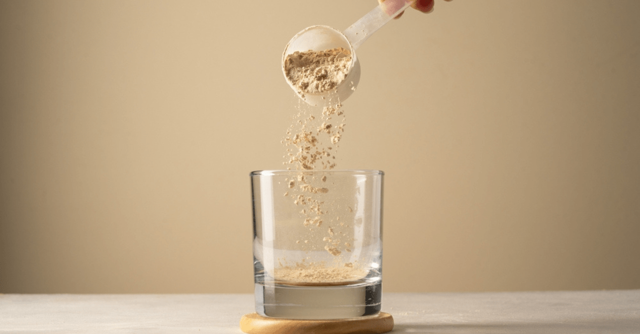 Pouring protein powder from scoop, in glass a glass. Making a protein drink.
