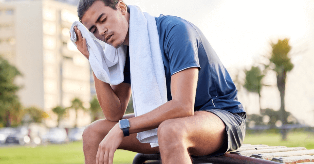 Fitness, exercise and tired man with a towel on park bench to relax or rest after running for cardio.