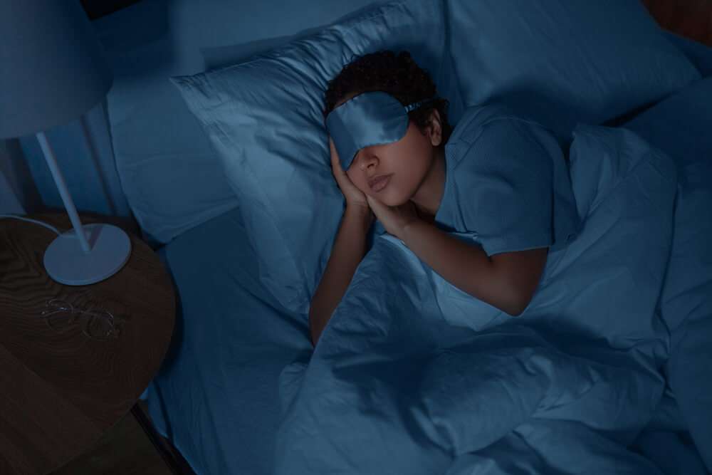 Young african american woman in eye mask sleeping in bed at home at night