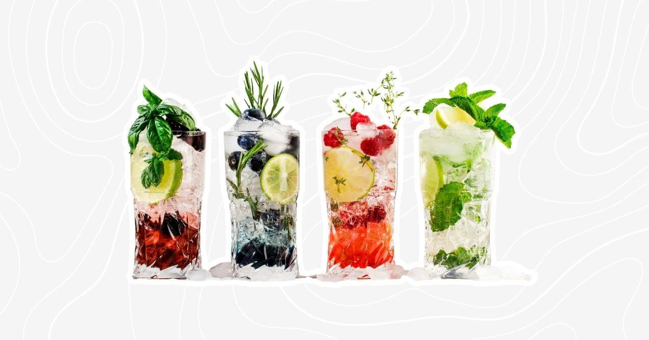 Four colorful mocktail glasses garnished with fresh herbs and fruits including mint, lime, blueberries, raspberries, and basil.