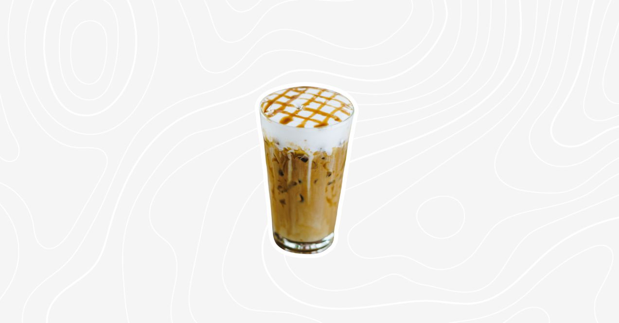 A tall glass of caramel iced mushroom coffee topped with a caramel drizzle and foam.