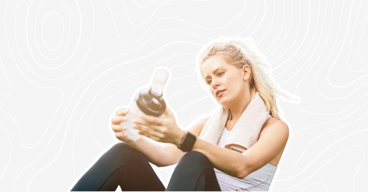 Woman sitting post-workout, holding a protein shaker bottle, with a towel draped around her neck.