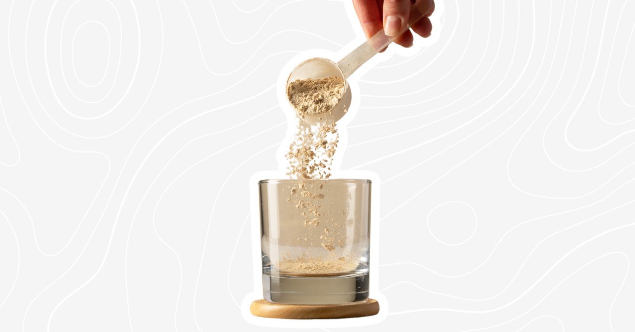 Scoop of protein powder being poured into a glass.