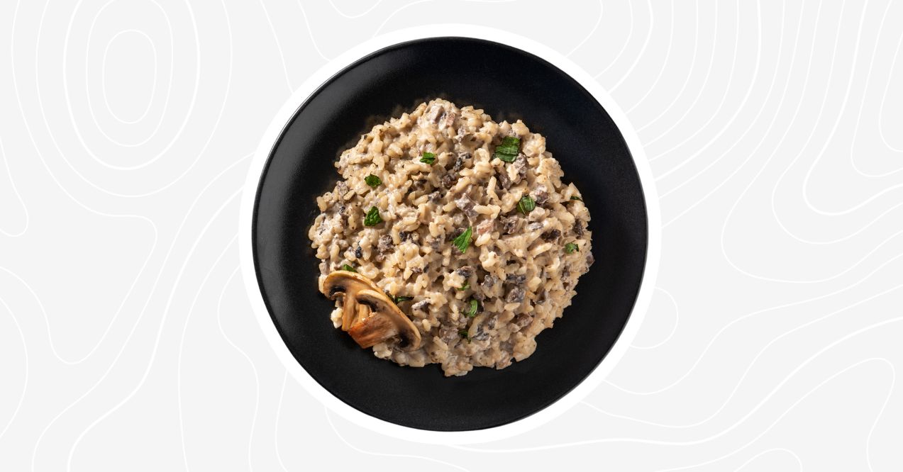 Creamy bone broth risotto served on a black plate, garnished with herbs and mushrooms.