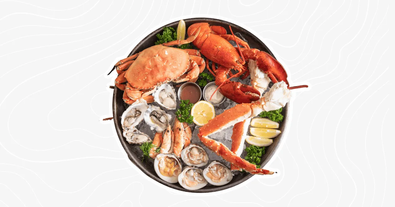 A seafood platter featuring a variety of shellfish, including crab, lobster, shrimp, oysters, and king crab legs, garnished with lemon slices and parsley.