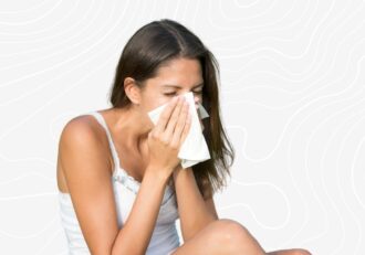 A female blowing her nose into a napkin due to allergy on the grey custom background